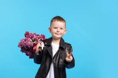 Photo of Little boy with bouquet of lilac flowers showing V-sign on light blue background