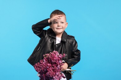 Photo of Little boy with bouquet of lilac flowers on light blue background