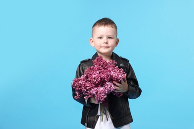 Photo of Little boy with bouquet of lilac flowers on light blue background