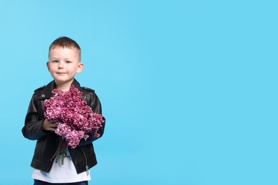 Photo of Little boy with bouquet of lilac flowers on light blue background, space for text