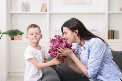 Photo of Mother and her son with bouquet of lilac flowers at home