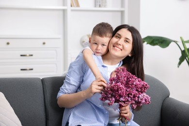 Photo of Mother and her son with bouquet of lilac flowers at home