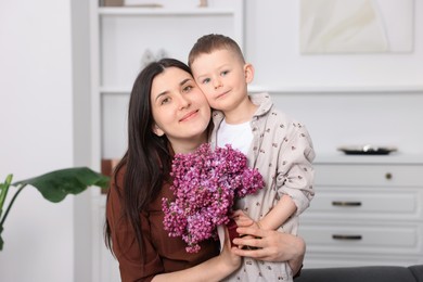 Photo of Mother and her son with bouquet of lilac flowers at home