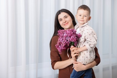 Photo of Mother and her son with bouquet of lilac flowers at home, space for text
