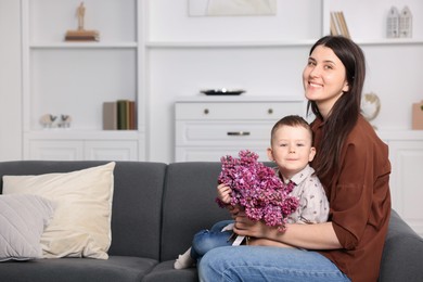 Photo of Mother and her son with bouquet of lilac flowers at home, space for text