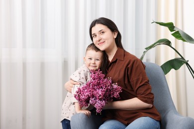 Photo of Mother and her son with bouquet of lilac flowers at home, space for text