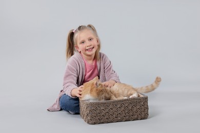 Photo of Little girl with her cute ginger cat on light grey background