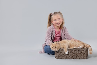 Photo of Little girl with her cute ginger cat on light grey background, space for text