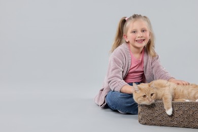 Photo of Little girl with her cute ginger cat on light grey background, space for text