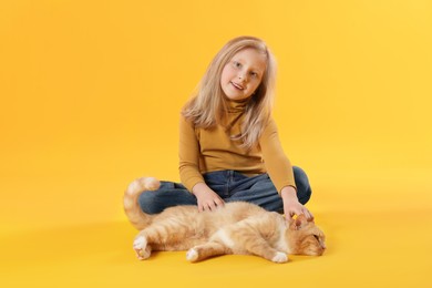 Photo of Little girl with her cute ginger cat on yellow background