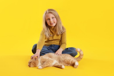 Photo of Little girl with her cute ginger cat on yellow background
