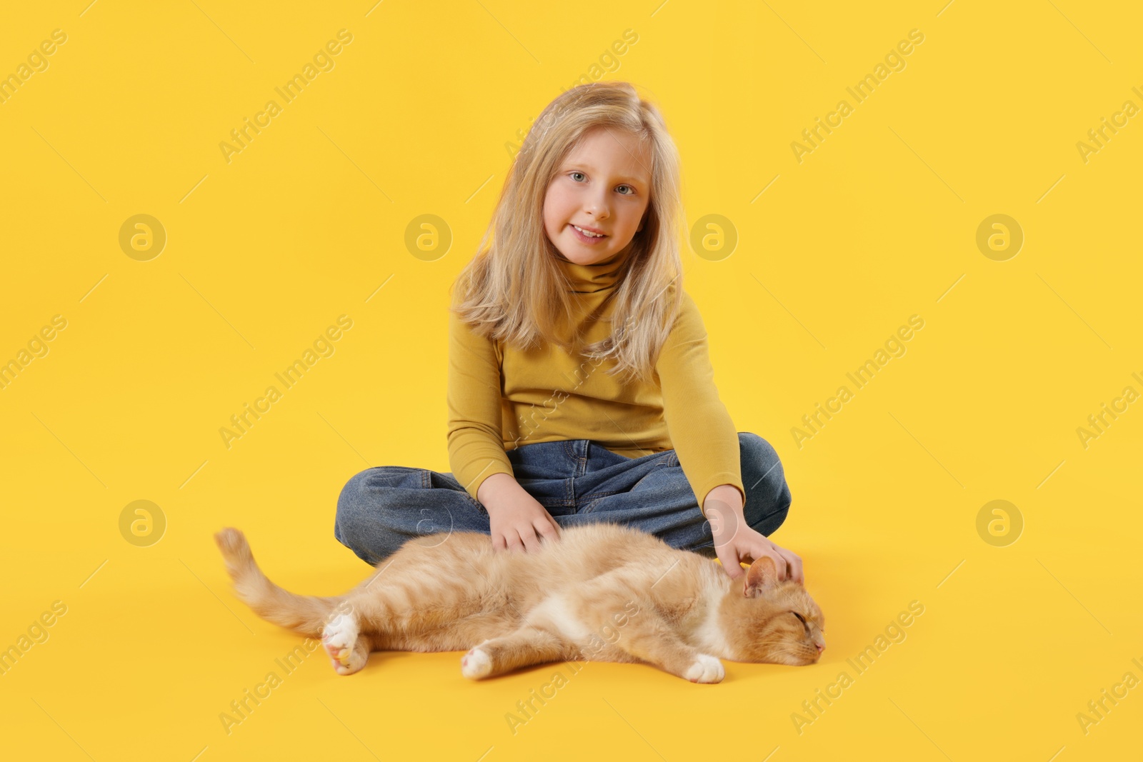 Little girl with her cute ginger cat on yellow background Photo of Little girl with her cute ginger cat on yellow background