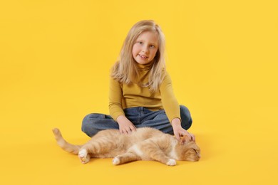 Photo of Little girl with her cute ginger cat on yellow background