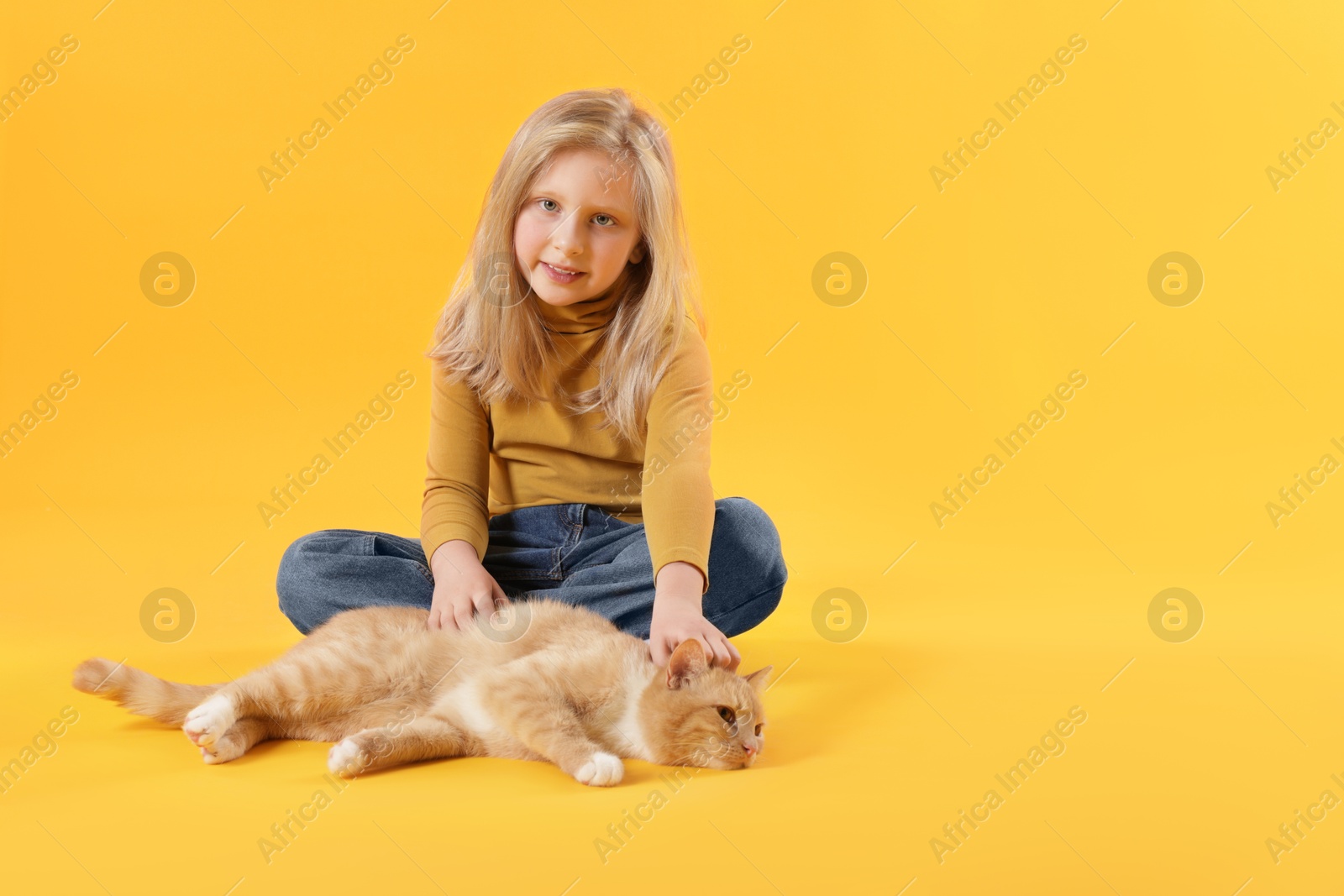 Little girl with her cute ginger cat on yellow background, space for text Photo of Little girl with her cute ginger cat on yellow background, space for text