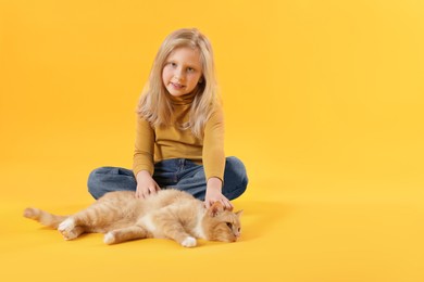 Photo of Little girl with her cute ginger cat on yellow background, space for text