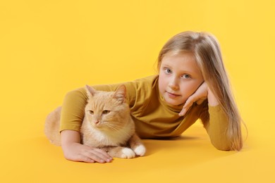 Photo of Little girl with her cute ginger cat on yellow background