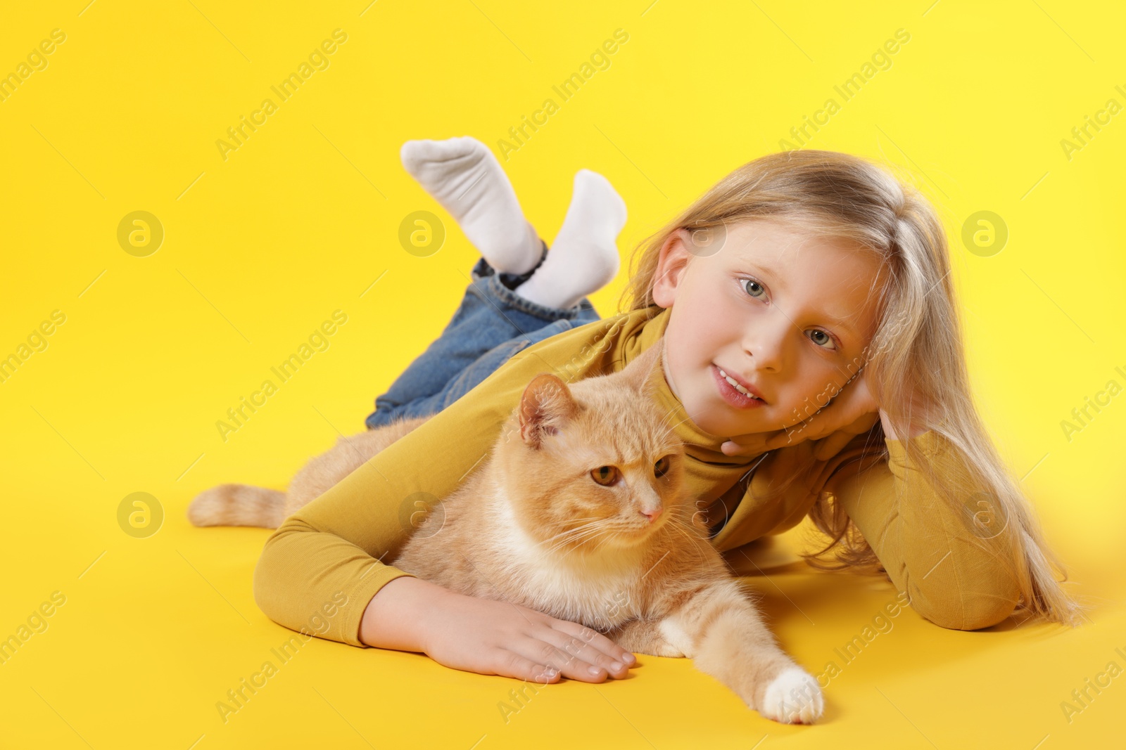 Little girl with her cute ginger cat on yellow background Photo of Little girl with her cute ginger cat on yellow background