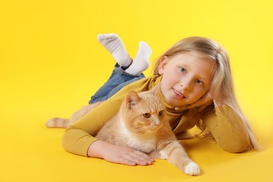 Photo of Little girl with her cute ginger cat on yellow background