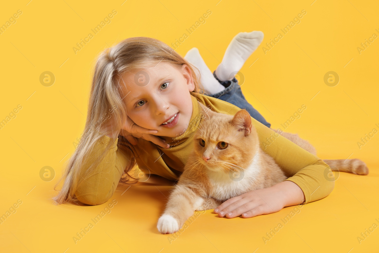 Little girl with her cute ginger cat on yellow background Photo of Little girl with her cute ginger cat on yellow background