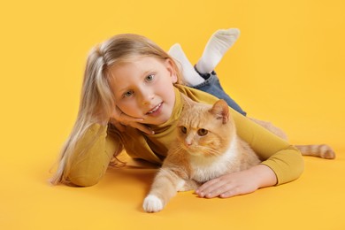 Photo of Little girl with her cute ginger cat on yellow background