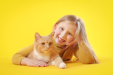 Photo of Little girl with her cute ginger cat on yellow background