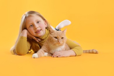 Photo of Little girl with her cute ginger cat on yellow background, space for text
