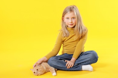 Photo of Little girl with her cute ginger cat on yellow background, space for text
