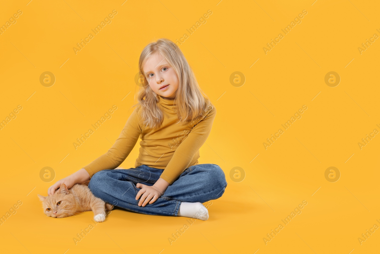 Little girl with her cute ginger cat on yellow background, space for text Photo of Little girl with her cute ginger cat on yellow background, space for text
