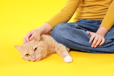 Photo of Little girl with her cute ginger cat on yellow background, closeup