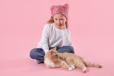Photo of Little girl with her cute ginger cat on pink background