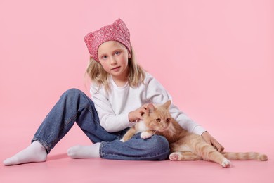 Photo of Little girl with her cute ginger cat on pink background