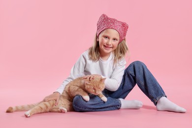 Photo of Little girl with her cute ginger cat on pink background