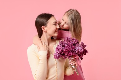 Photo of Mother and her daughter with bouquet of lilac flowers on pink background