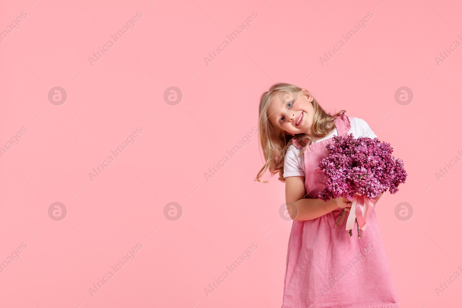 Little girl with bouquet of lilac flowers on pink background, space for text Photo of Little girl with bouquet of lilac flowers on pink background, space for text