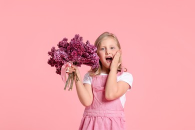 Photo of Surprised little girl with bouquet of lilac flowers on pink background