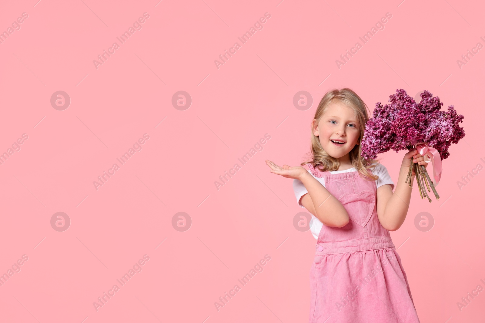 Little girl with bouquet of lilac flowers on pink background, space for text Photo of Little girl with bouquet of lilac flowers on pink background, space for text
