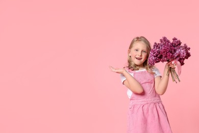 Photo of Little girl with bouquet of lilac flowers on pink background, space for text