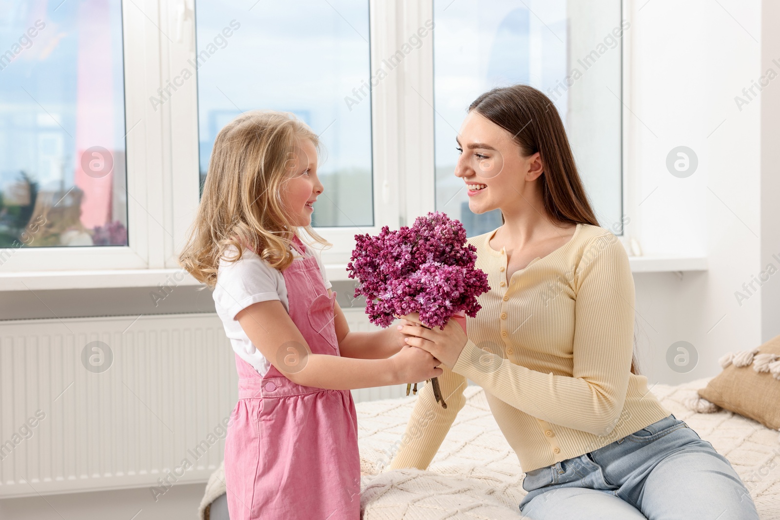 Mother and her daughter with bouquet of lilac flowers at home Photo of Mother and her daughter with bouquet of lilac flowers at home