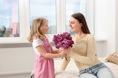 Photo of Mother and her daughter with bouquet of lilac flowers at home