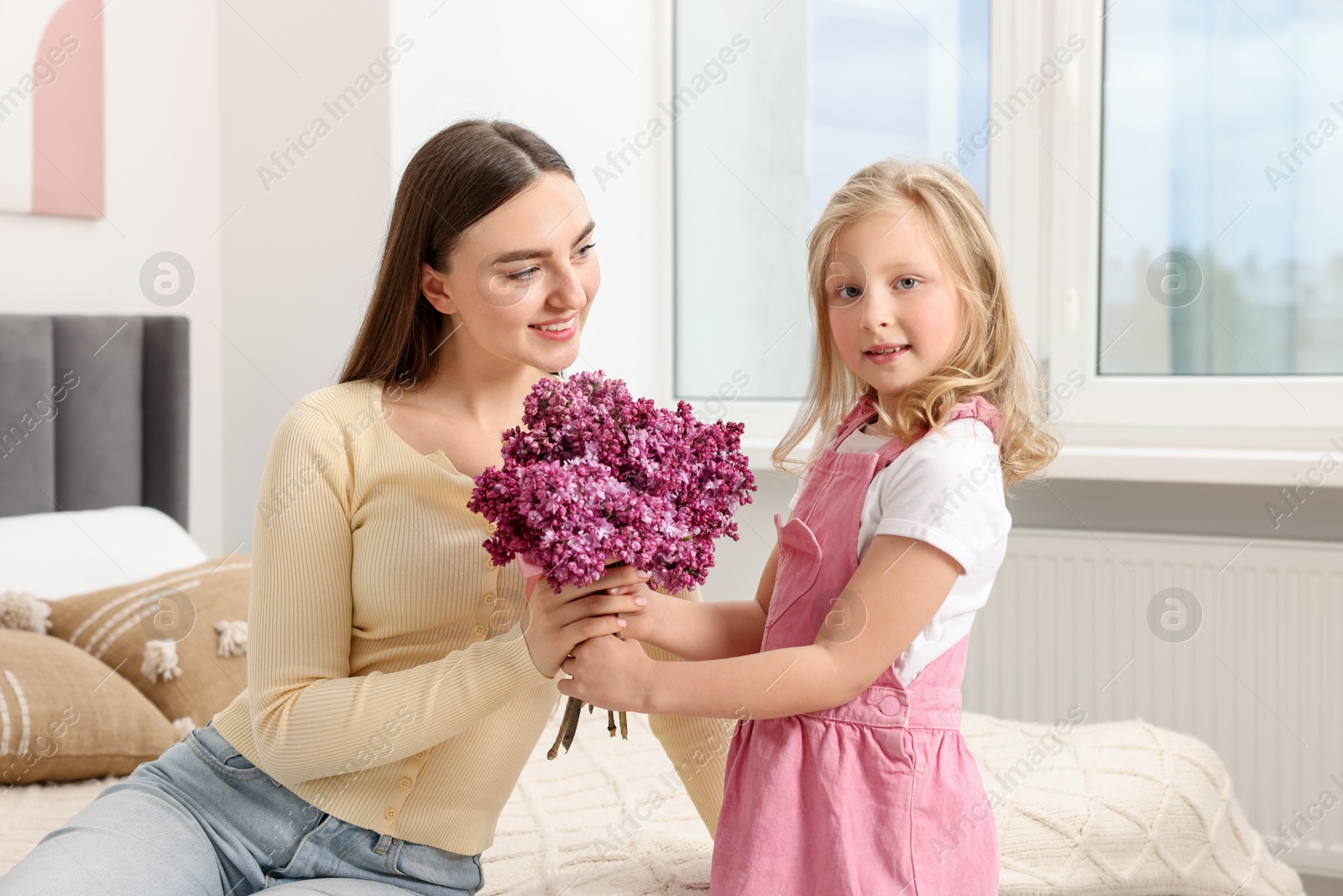 Mother and her daughter with bouquet of lilac flowers at home Photo of Mother and her daughter with bouquet of lilac flowers at home