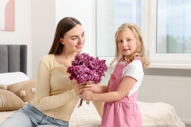 Photo of Mother and her daughter with bouquet of lilac flowers at home