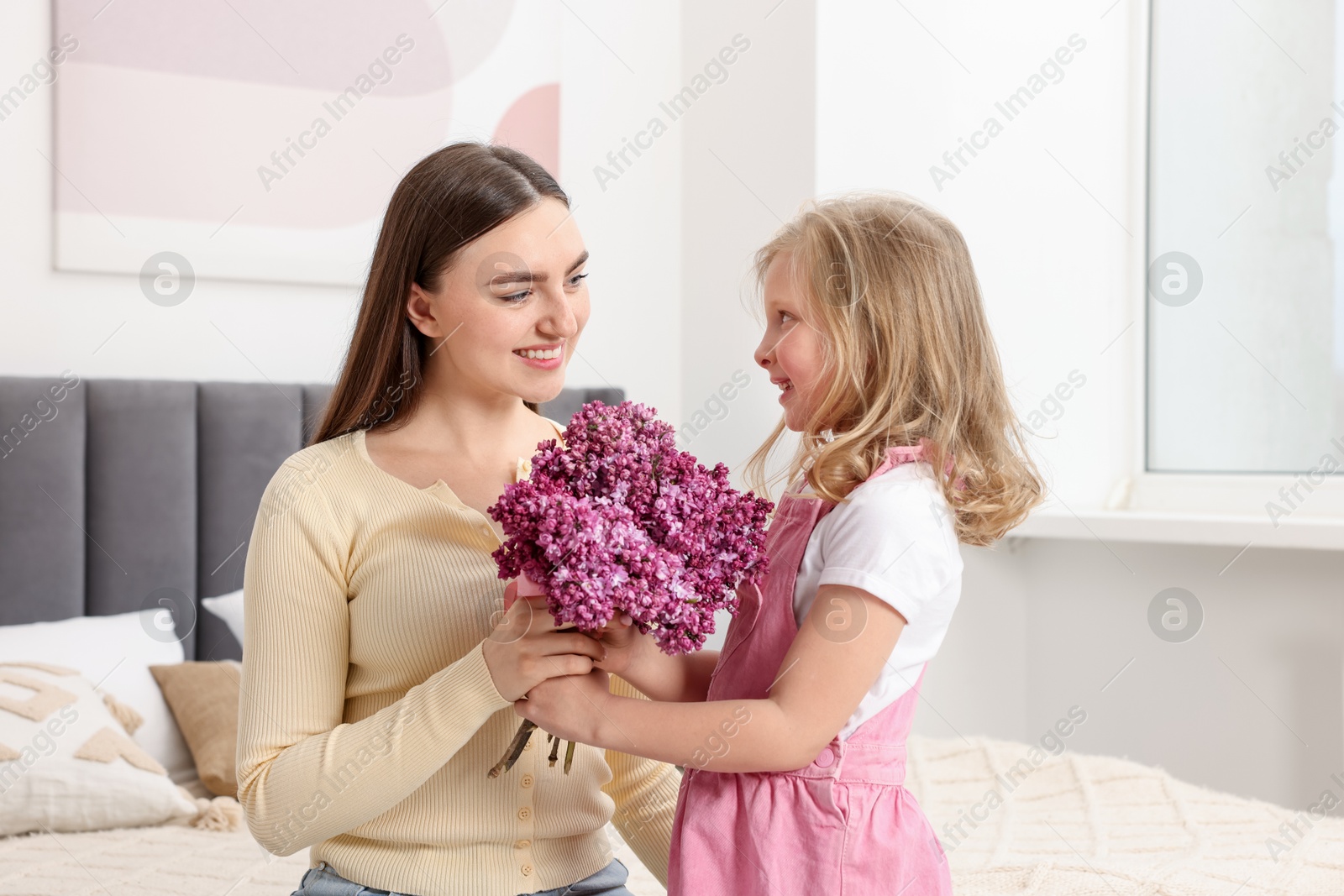 Mother and her daughter with bouquet of lilac flowers at home Photo of Mother and her daughter with bouquet of lilac flowers at home