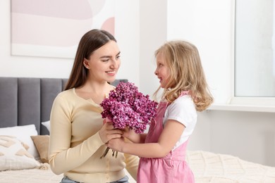 Photo of Mother and her daughter with bouquet of lilac flowers at home
