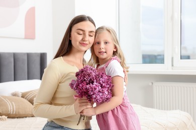 Photo of Mother and her daughter with bouquet of lilac flowers at home