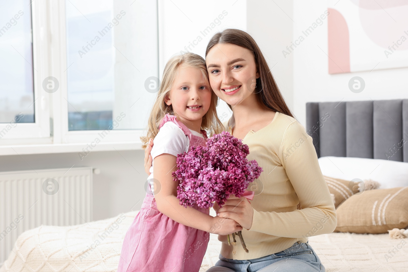 Mother and her daughter with bouquet of lilac flowers at home Photo of Mother and her daughter with bouquet of lilac flowers at home