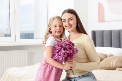 Photo of Mother and her daughter with bouquet of lilac flowers at home