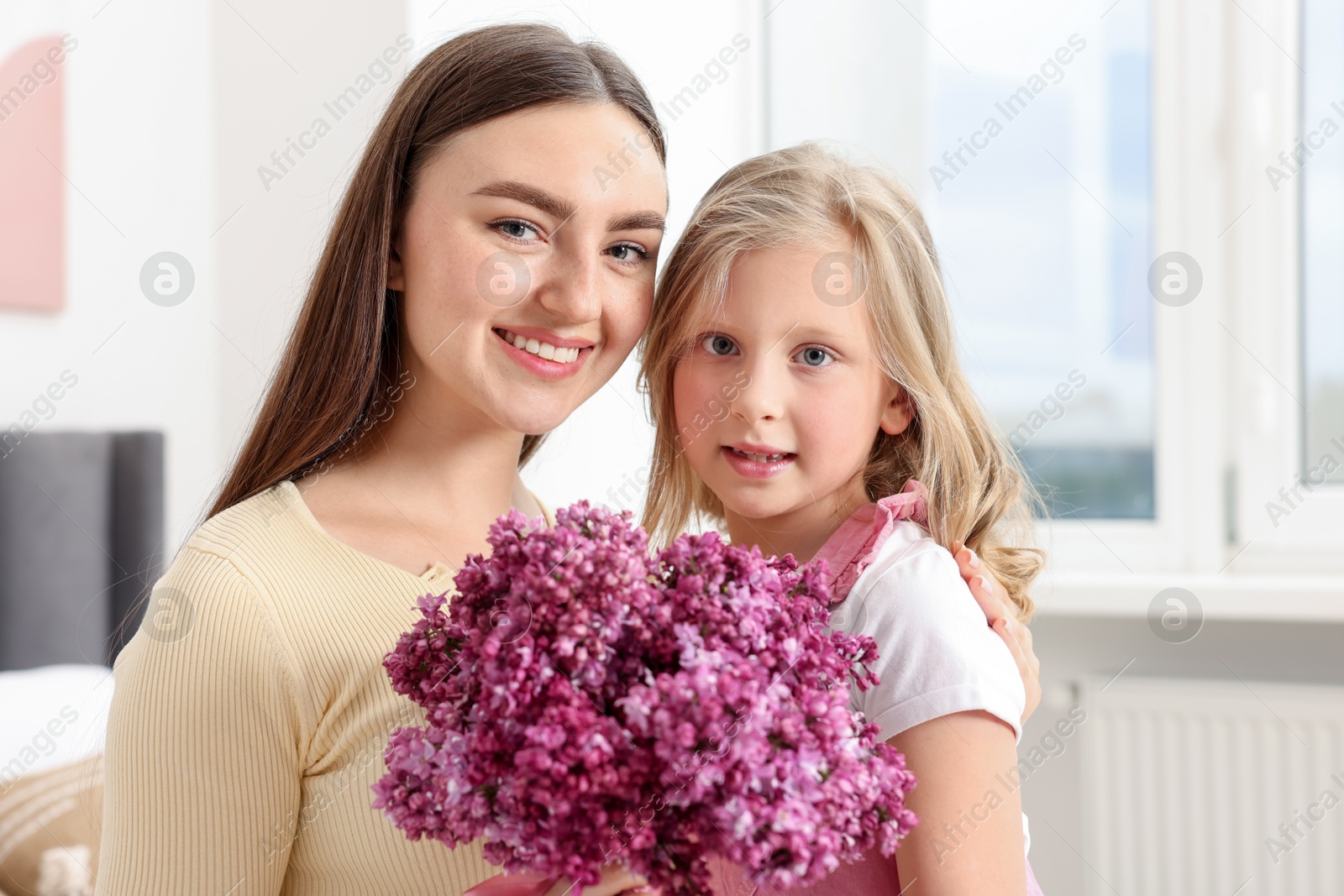 Mother and her daughter with bouquet of lilac flowers at home Photo of Mother and her daughter with bouquet of lilac flowers at home