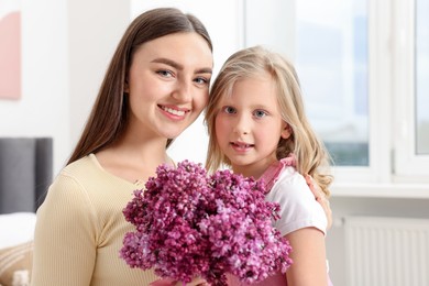 Photo of Mother and her daughter with bouquet of lilac flowers at home