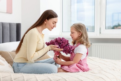 Photo of Mother and her daughter with bouquet of lilac flowers at home