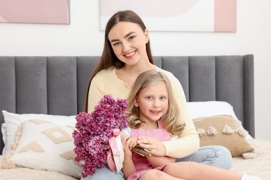 Photo of Mother and her daughter with bouquet of lilac flowers at home